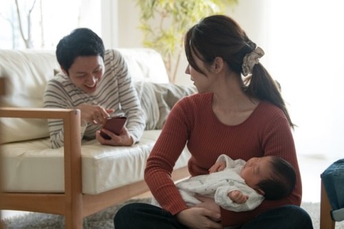 Woman caring for baby while man plays games