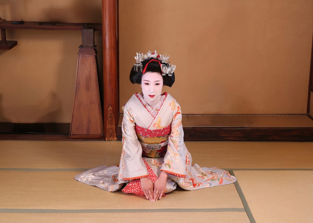 A maiko in Kyoto's Gion district bowing on a tatami mat.