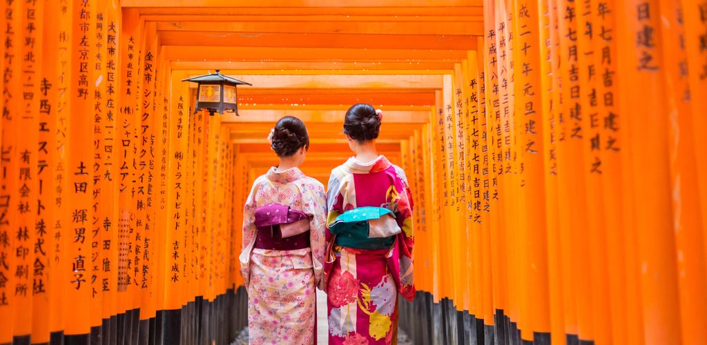 Two geish seen from behind walking through the torii at Fushimi-Inari Taisha in Kyoto