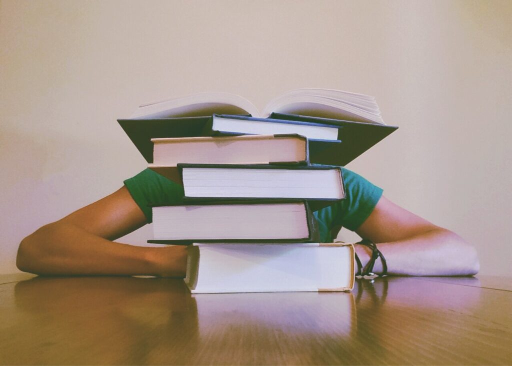 Image of student with head down behind a stack of books - cram for the JLPT exam