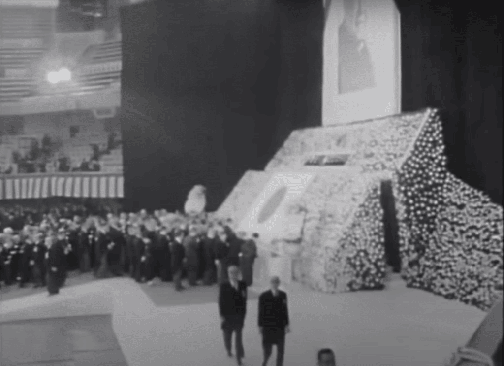 Mourners at the state funeral of Yoshida Shigeru pay their respects in front of a large display of flower upon which rests the rising sun flag.