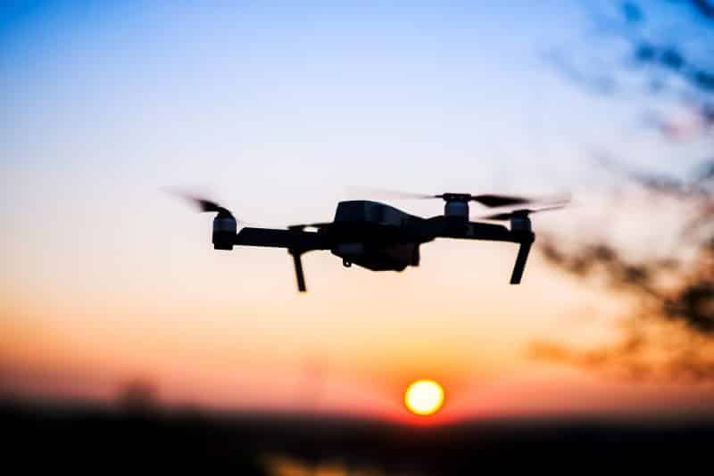 Flying drone into the sunset. Silhouette against sun. Quad copter in motion.