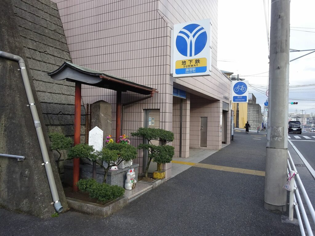 A small shinto shrine with a manekineko, representing bakeneko cats, next to an entrance to Odoriba station.