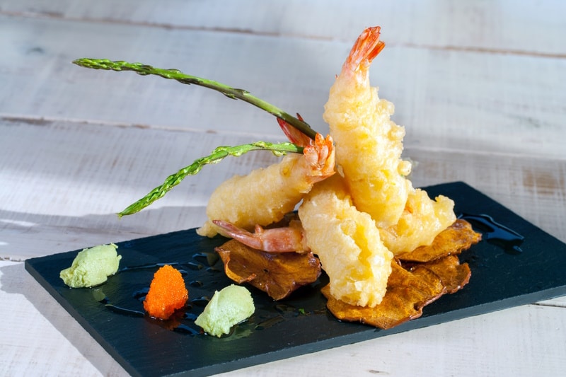 Close up of shrimp tempura appetiser served on black tile.