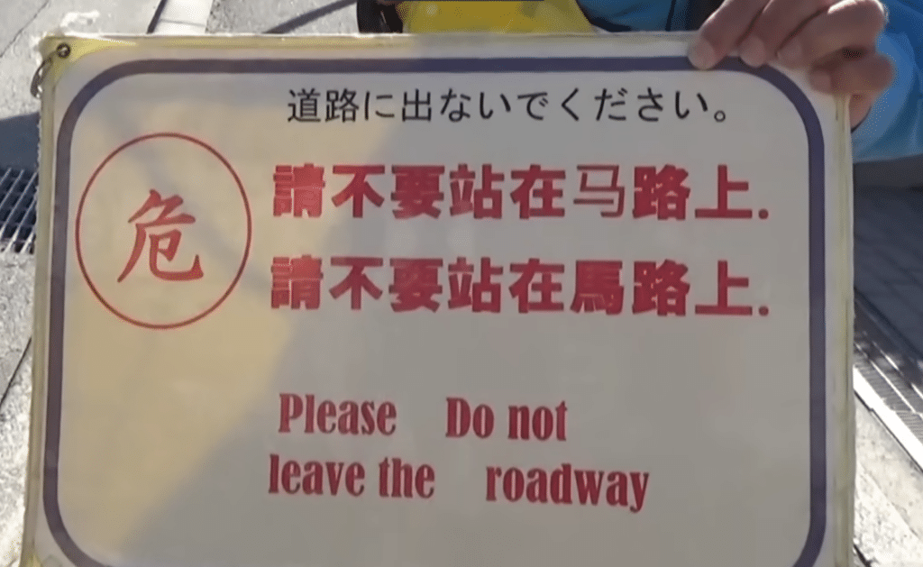 A sign telling trourists not to enter the roadway (though misworded in English as "Please do not leave the roadway")