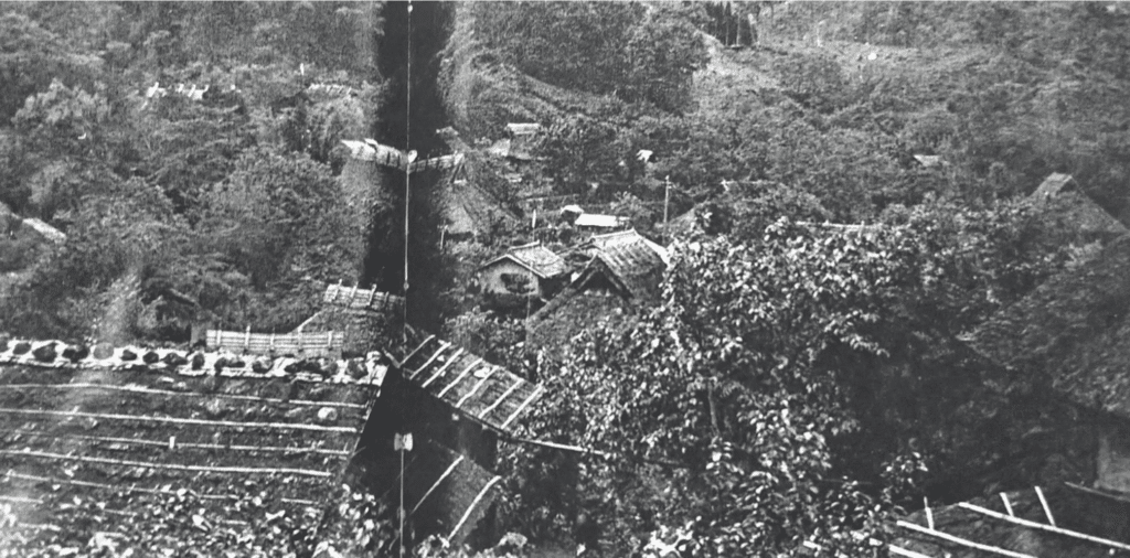 A black and white image of thatched-roof houses amidst a forest. City where the Tsyuama Massacre occurred.