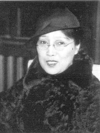 Tamura Toshiko portrayed in a black and white photograph, dressed in a black fur coat and cap, with glasses affixed.