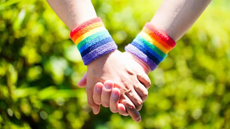 Two people with LGBTQ wrist bands holding hands