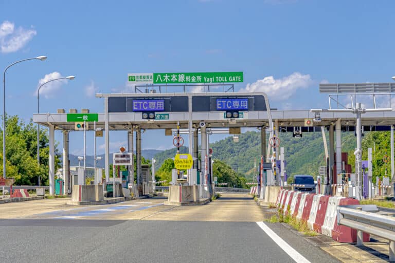 Toll road in Japan with green mountains and blue sky in the background.