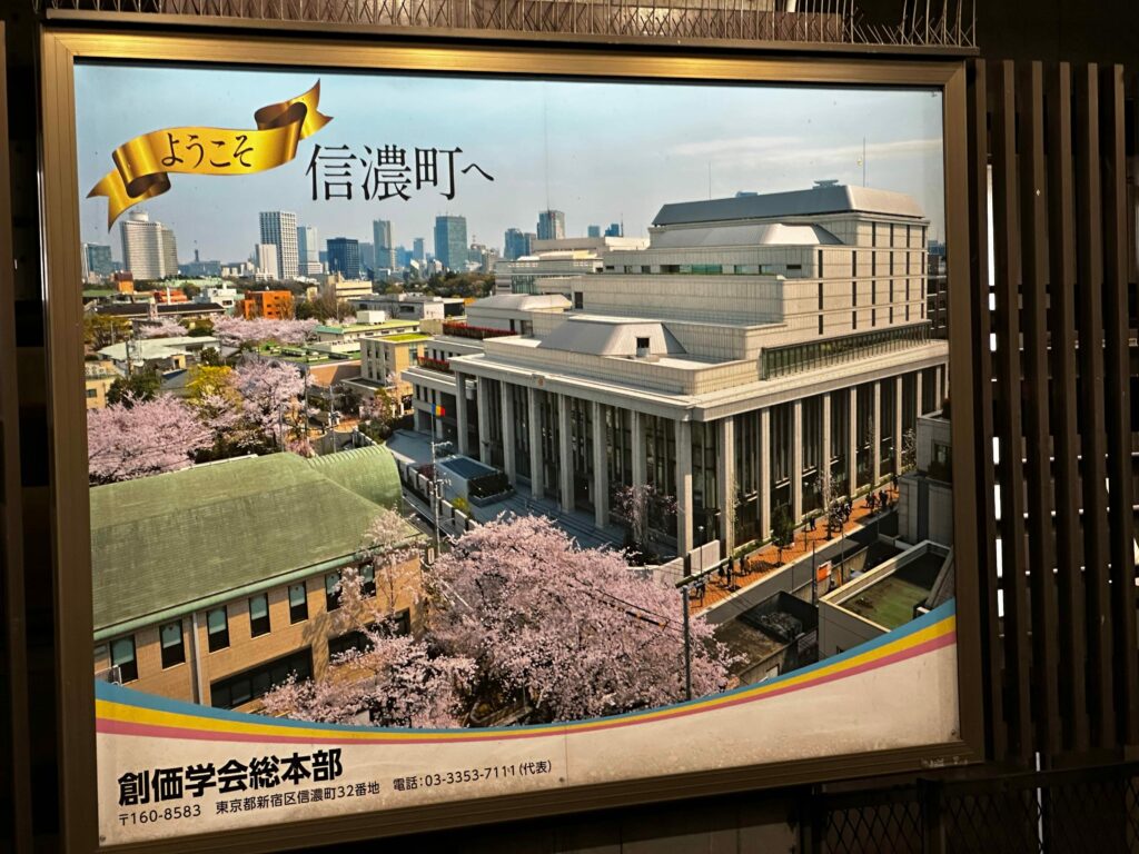 Poster of Soka Gakkai HQ in Shinanomachi, with white columns, tiered top floors, and cherry trees in bloom out front.