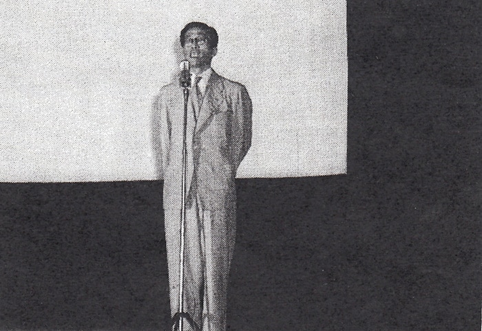 Young Uno Sosuke, standing in a suit in front of a microphone.