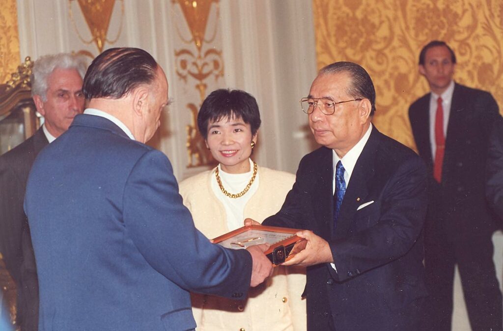 Ikeda Daisaku in navy suit accepting a plaque from a Russian man. Russian and Japanese figures watch on in a well-appointed room.