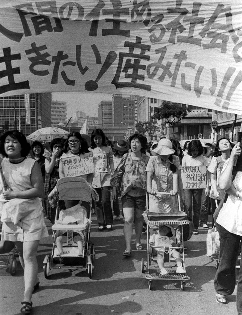 Japanese women with placards and baby prams march against a Japanese sterilization bill. Photograph is in black and white.