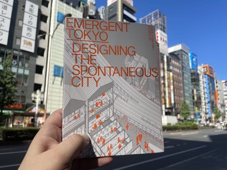 The book Emergent Tokyo held in front of a line of Zakkyo buildings on Tokyo's Yasukuni Street.