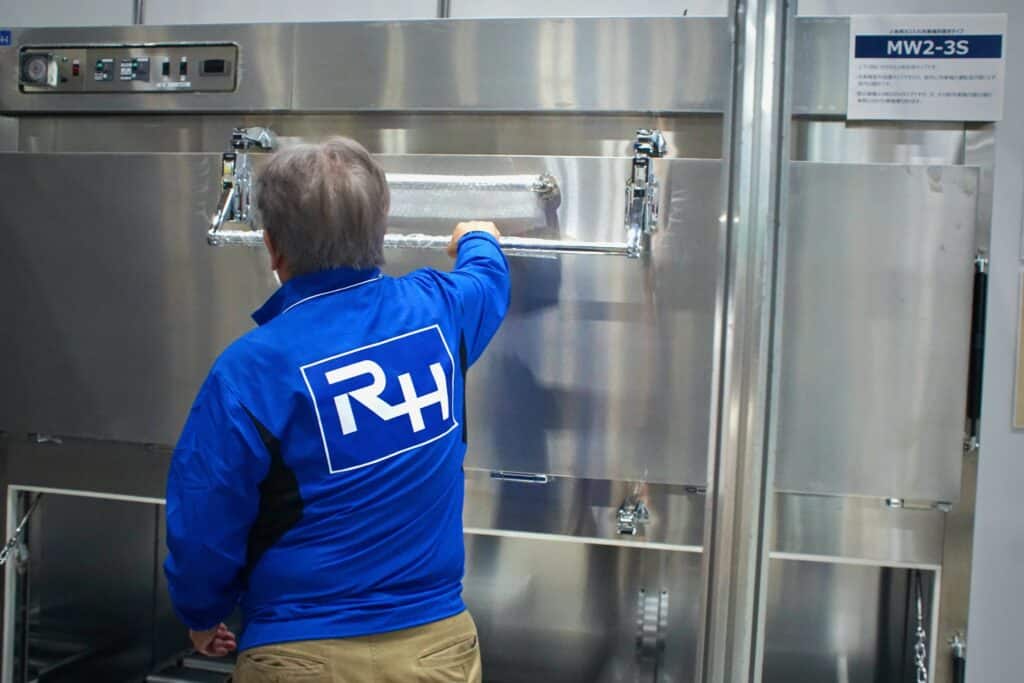 A man in a blue jumper opens a long metalic door to a refrigerator meant to contain the newly deceased at ENDEX.
