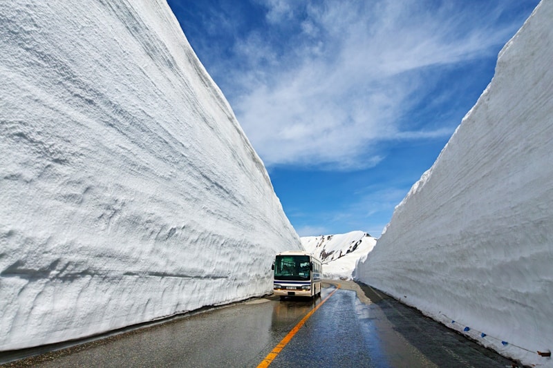 Bus driving through two huge snow piles that dwarf it by close to three times the height of the bus