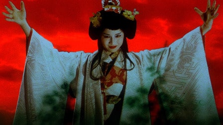 A woman in white kimono and elaborate hair with arms outstretched and a maniacal look on her face in the film House.