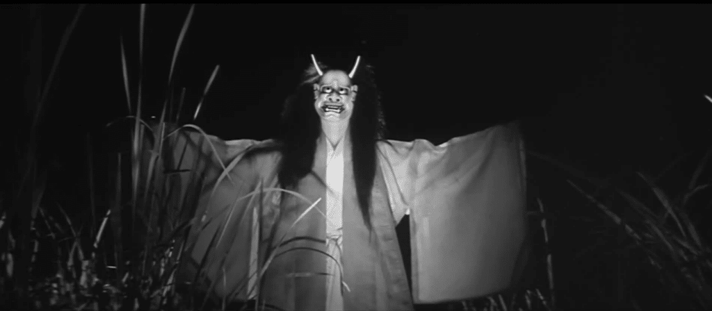 A ghostly figure in kimono and a demonic noh mask emerges from the tall grass in the film Onibaba.