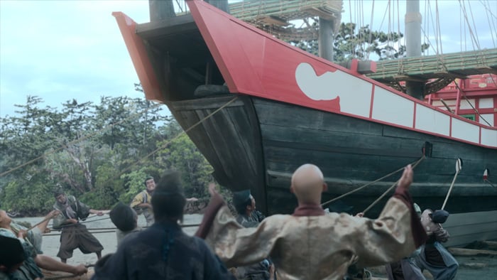 A large, angular wooden ship, build on the orders of Minamoto no Sanetomo, is pulled out to sea by many men in period clothing.