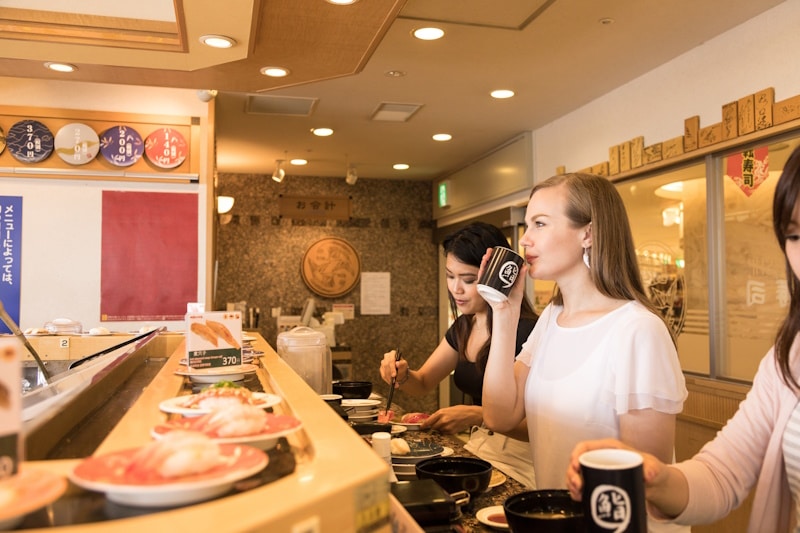 Woman drinking tea from cup at a conveyor sushi belt counter