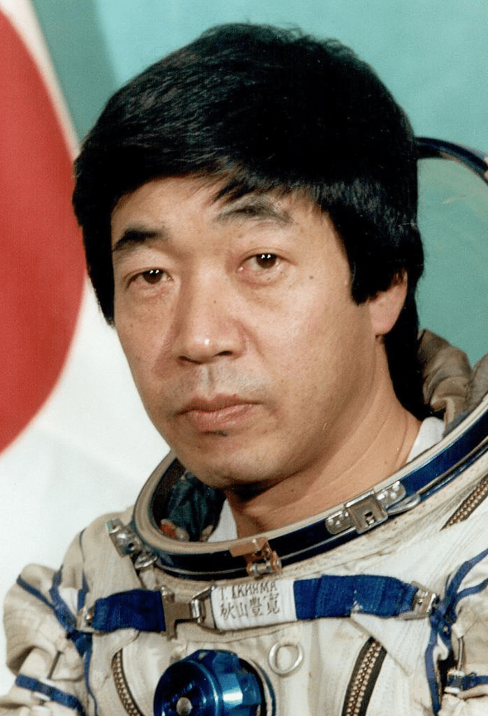 Akiyama Toyohiro, first Japanese astronaut in space suite with Japanese flag behind him.
