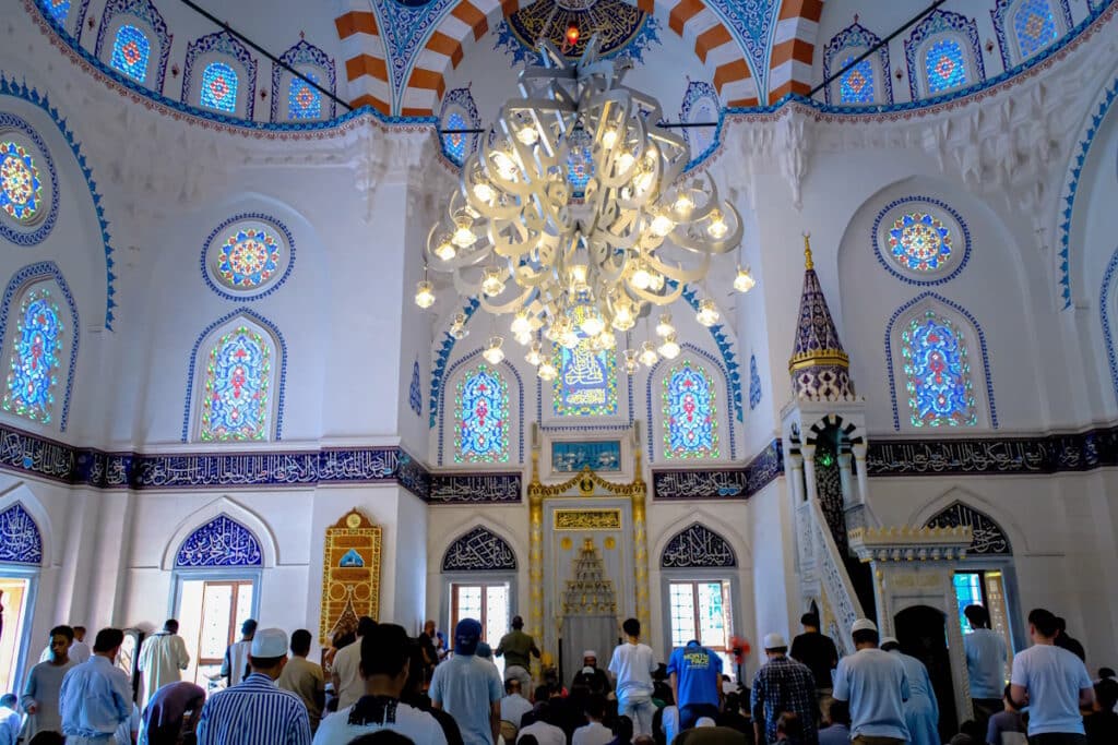Worshippers inside the prayer hall of Tokyo Camii, the Turkish mosque in Tokyo, with stained glass windows and a domed ceiling
