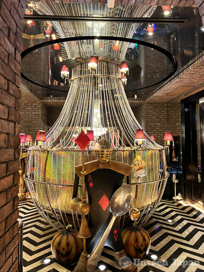 Old Castle Alice - table with beads stringing down along its sides in a flaring funnel shape, with an Ace of Diamonds guard with a helmet, a lanyard, and a spoon standing on guard