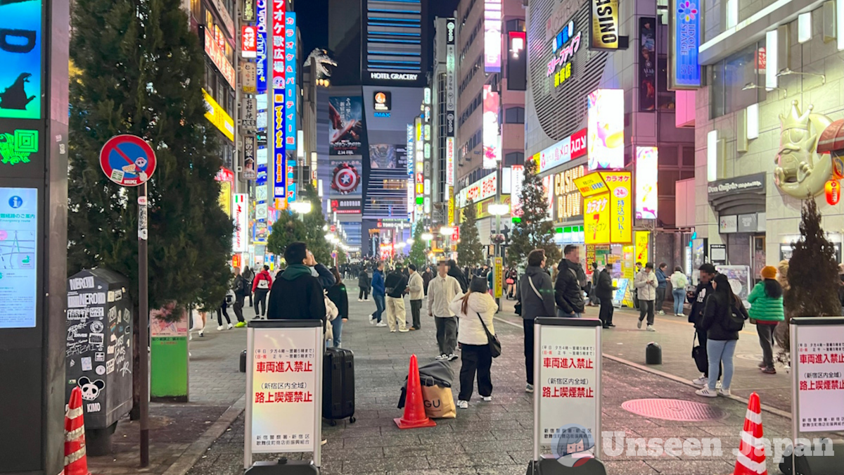 Toyoko, Kabukicho - shot of the area standing in front looking towards Toho Cinemas, Multiple visitors are walking and standing around on the brightly-lit neon street. You can see the Toho Godzilla in the background peering over the Hotel Gracery.