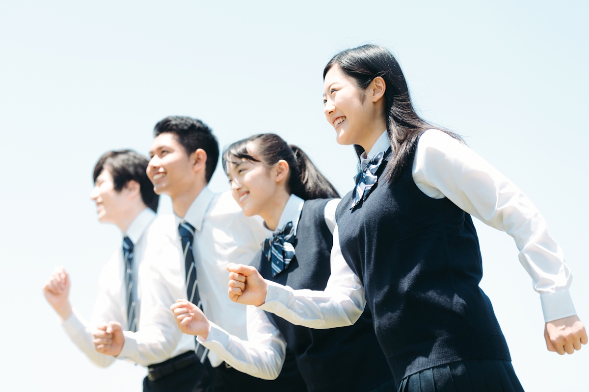 Four high school students running towards the left, staggered from left to right with two boys in back and two girls in front