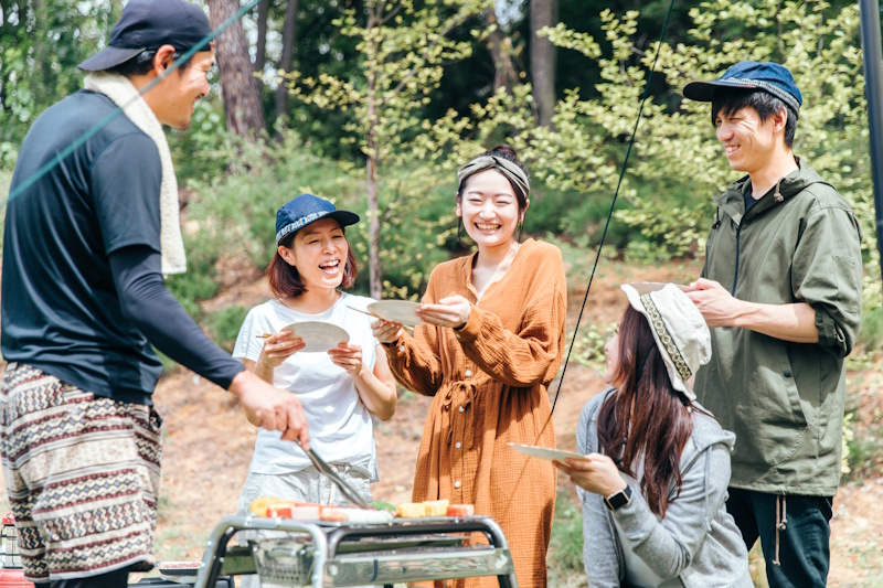 Five Japanese people standing around a grill while one cooks and the other four laugh and wait for food