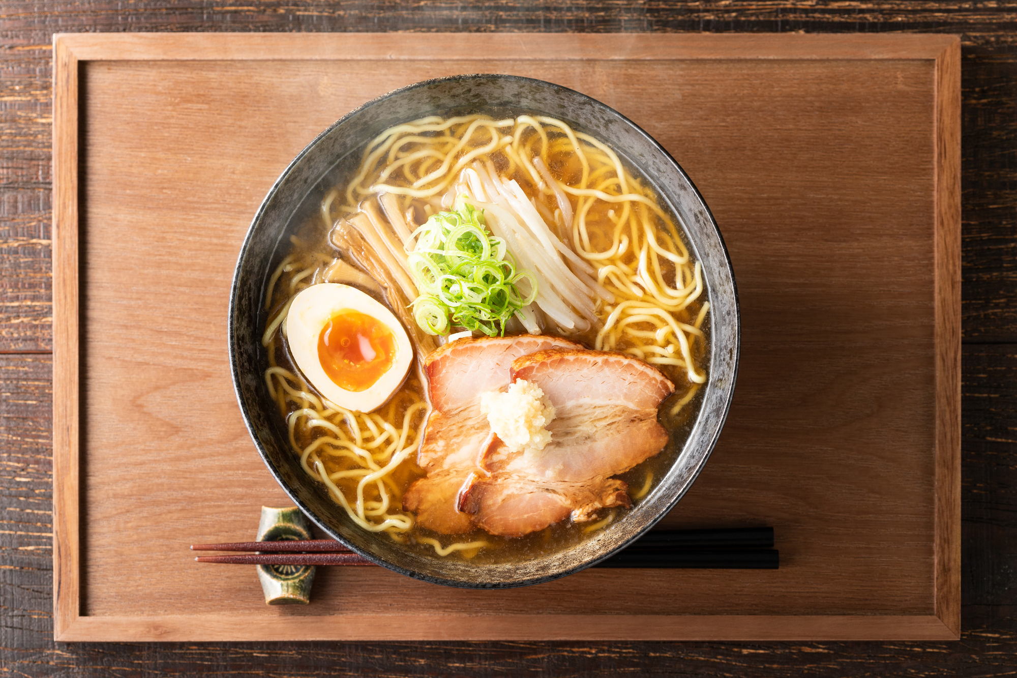A bowl of ramen neatly arranged on a brown wooden tray with a set of chopsticks set near the bottom of the bowl