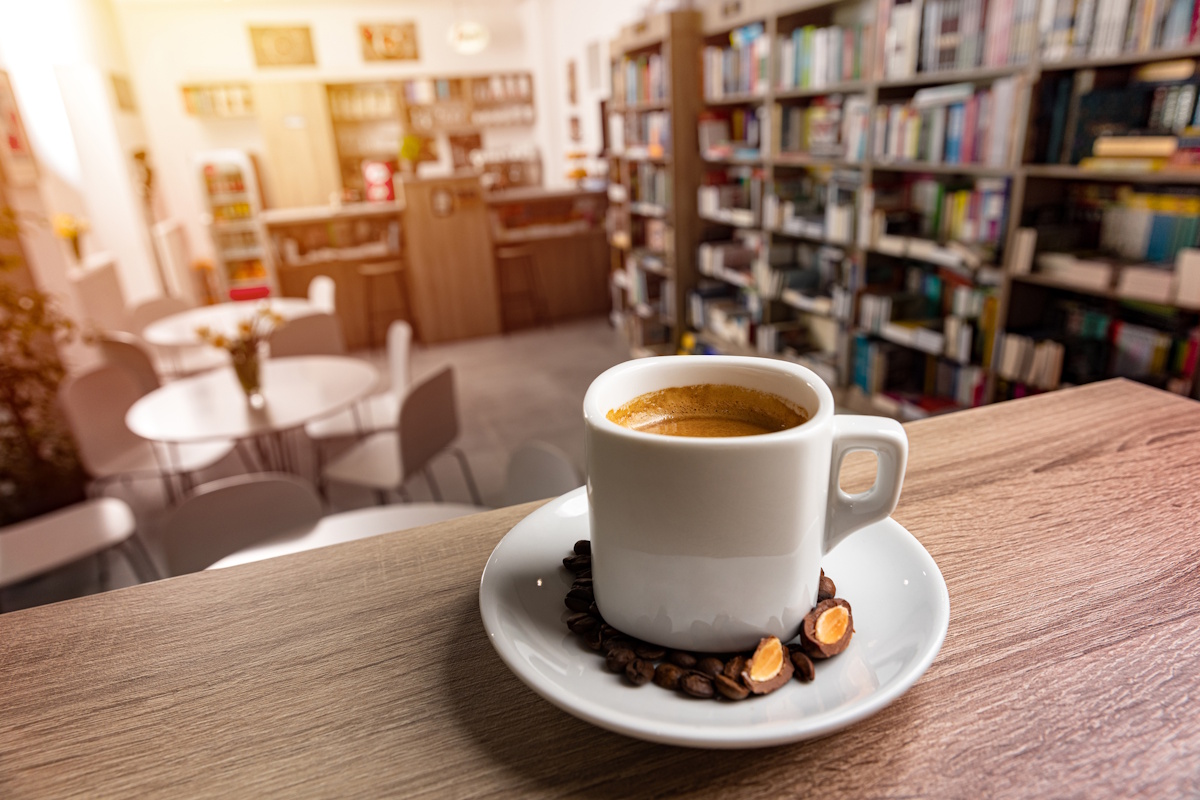 White cup of coffee with a saucer on table, blur bookstore background