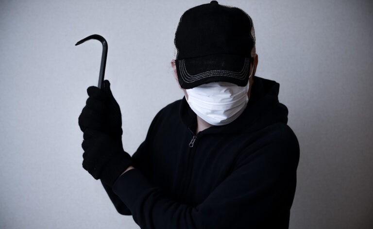 Picture of a man holding a crowbar about to break into a home