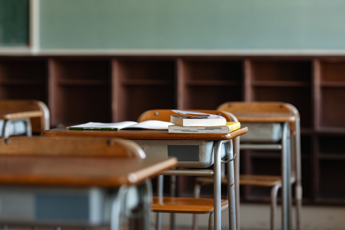 Close up of three or so desks in a school, with books on one of the desks