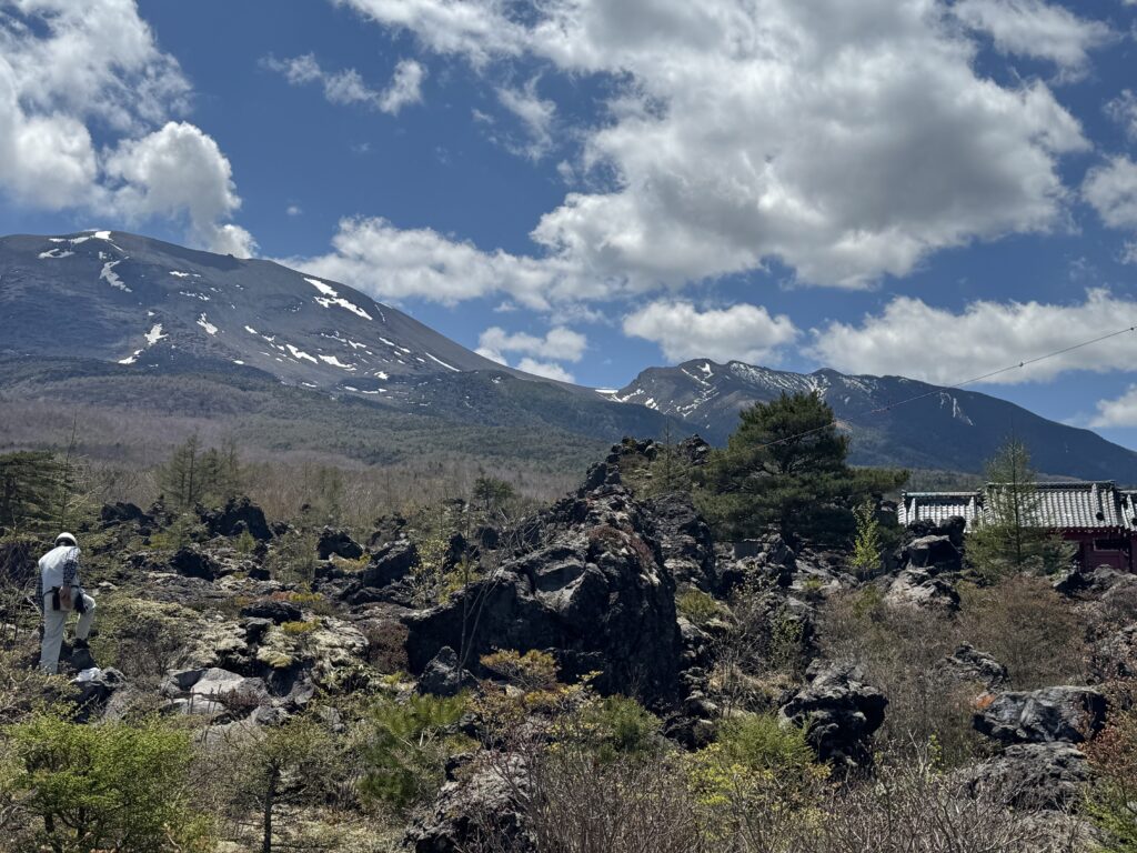 Volcanic and crags in front of a mountain range, with a blue sky filled with white clouds.