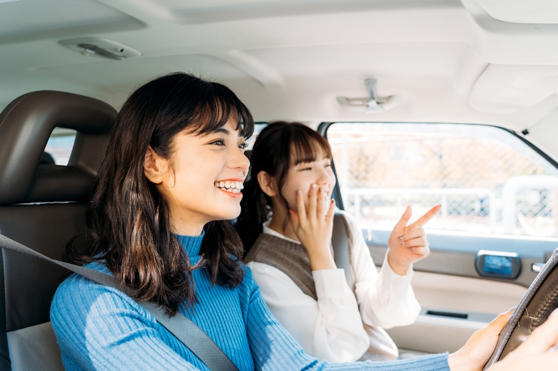 Woman driving while her friend holds one hand to her mouth and us using the other to point forward
