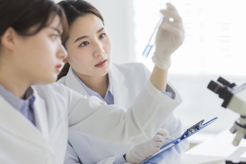 Two women in lab coats looking at a test tube vial