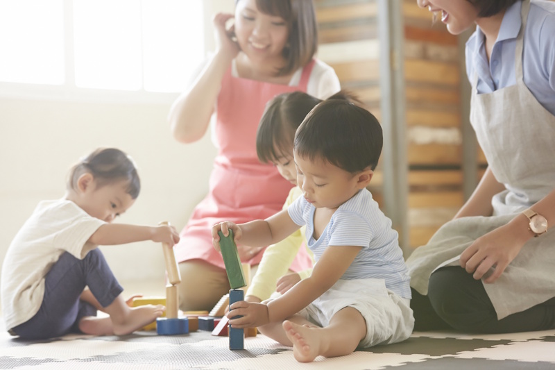 Children in a nursery school playing as caregivers look on, smiling