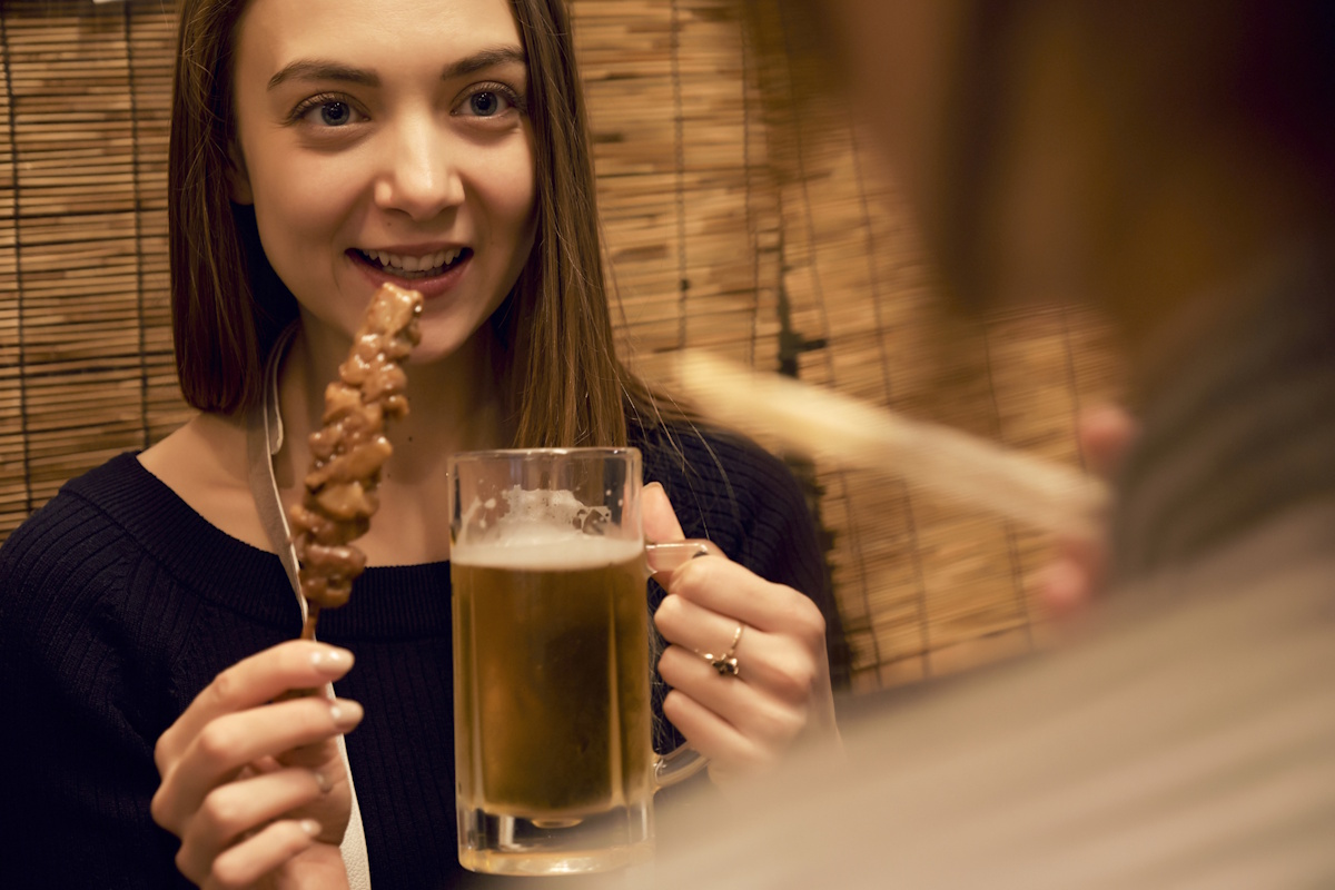 A woman eating kushiyaki and drinking a beer at a restaurant