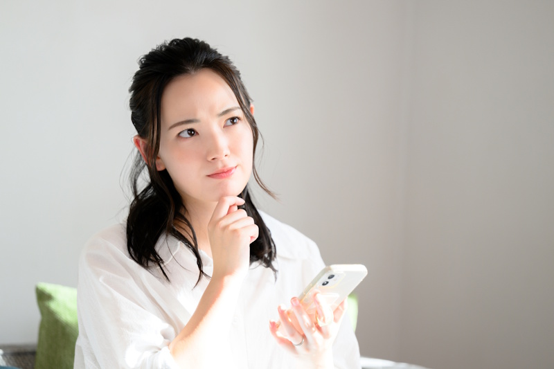 Woman looking thoughtful while using her smartphone (Japanese phone number article)