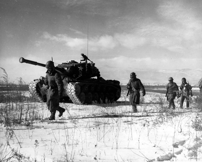 Soldiers marching beside a tank in the snow during the Korean War.