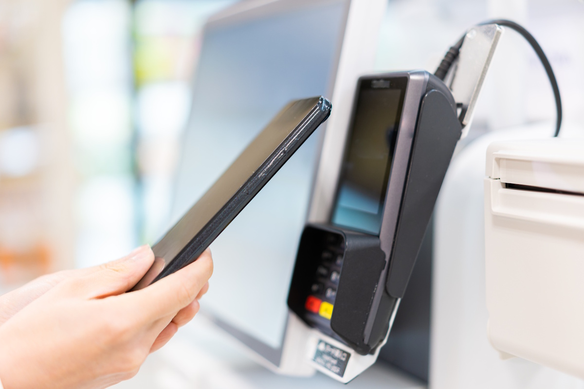 Hand holding up a phone to a self-checkout point of sale pad