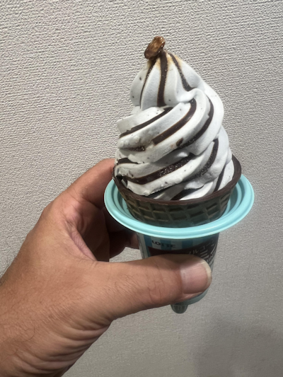 A hand holding Lotte's chocolate mint soft-serve ice cream in a chocolate-striped cup.