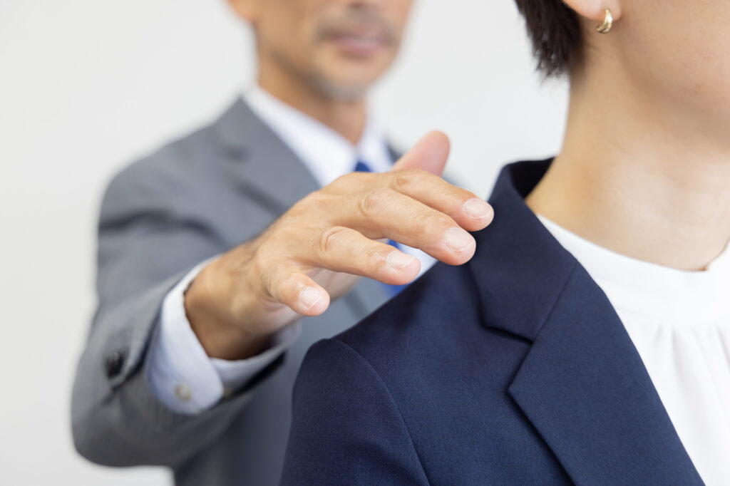 A man in a suit reaching to touch a female coworker's shoulder, illustrating workplace sexual harassment.