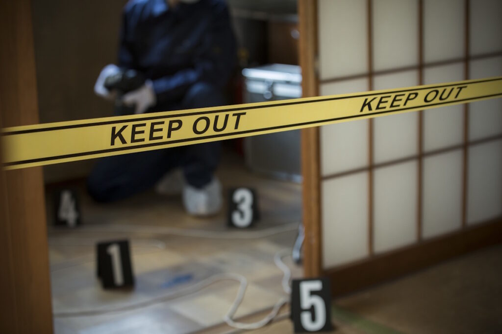 Forensic examiner takes pictures of a crime scene. Yellow KEEP OUT tape can be seen in the foreground