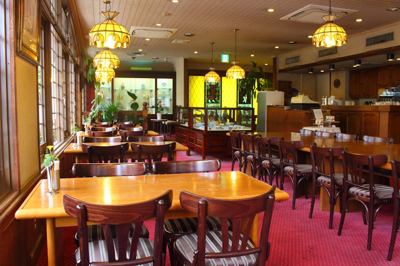 Interior of a traditional Japanese kissaten with Tiffany-style pendant lamps, wooden tables, and red carpeting.