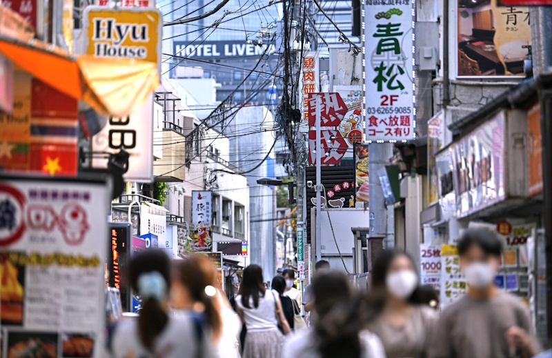 A crowded Tokyo restaurant alley lined with brightly colored Japanese-language signs and storefronts.