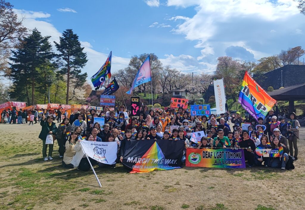 Participants pose for a group photo with Pride flags and banners from Akita Pride March, Deaf LGBT Tohoku, and other organizations
