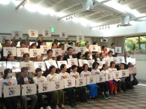 About fifty people hold white placards naming Japanese prefectures, each with a rainbow 'YES!' marriage-equality logo.