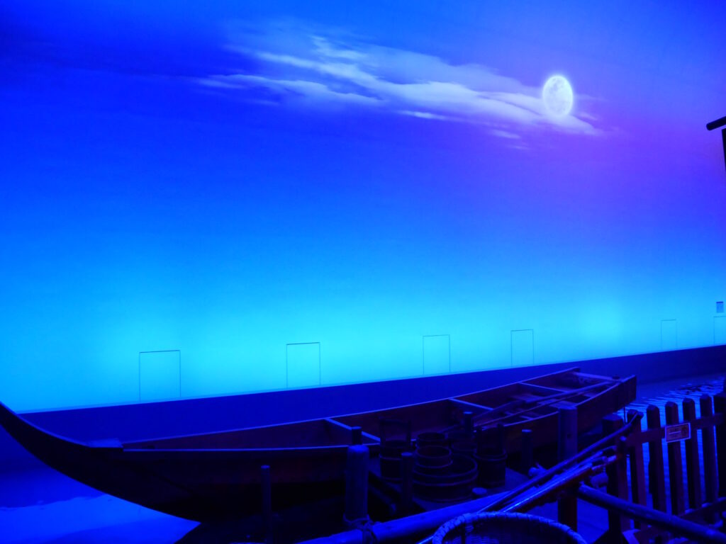 Wooden flat-bottomed boat on a recreated canal under a painted night sky and moon at the Fukagawa Edo Museum